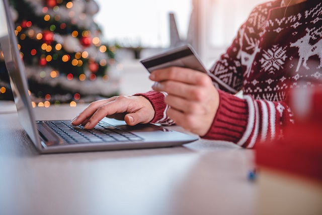 Woman in red Christmas jumper shopping on laptop with credit card. Online security concept for Intersys