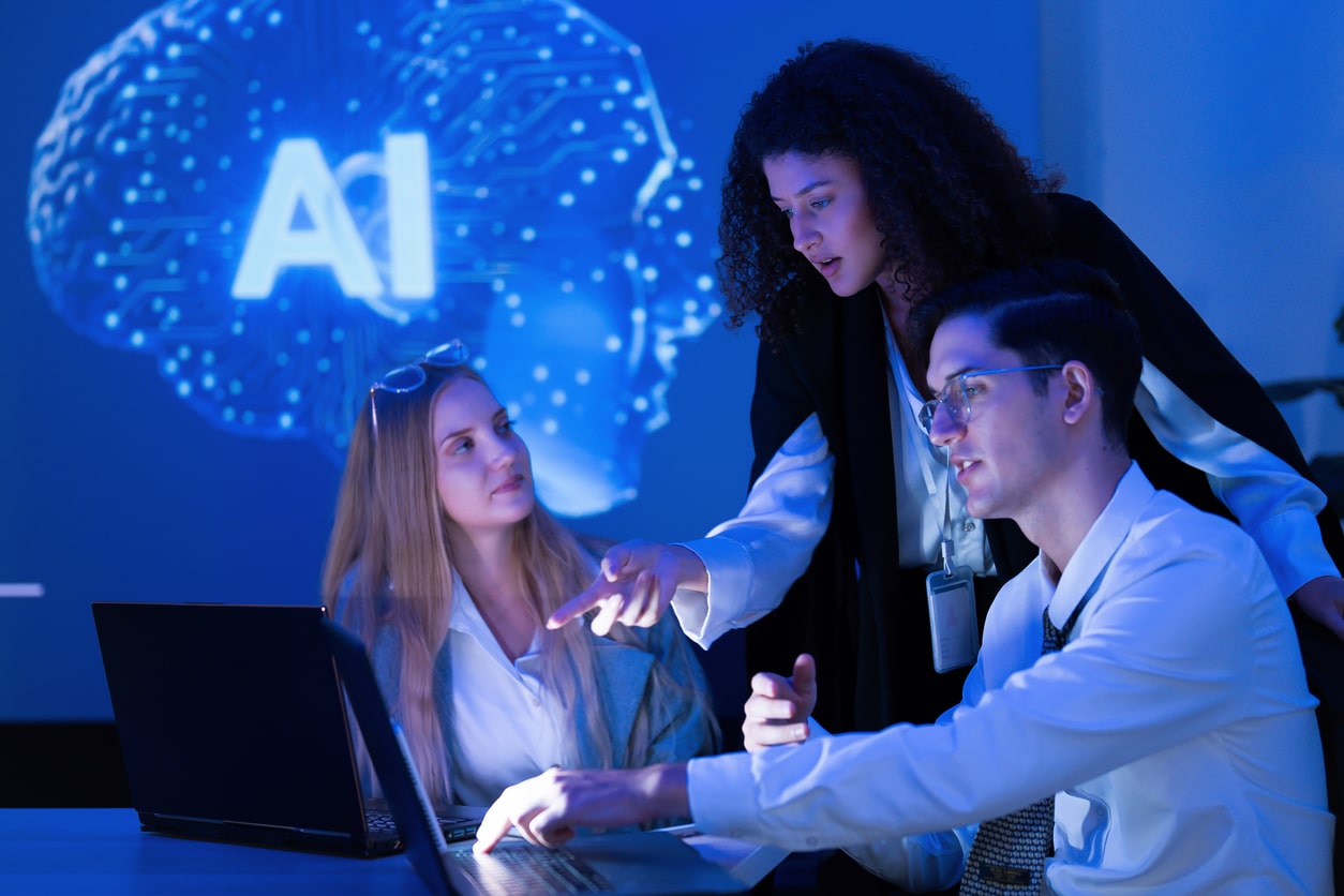 Team of office workers conferring around a computer screen with a graphic saying 'AI in the background. Illustrating the concept of AI governance for Intersys