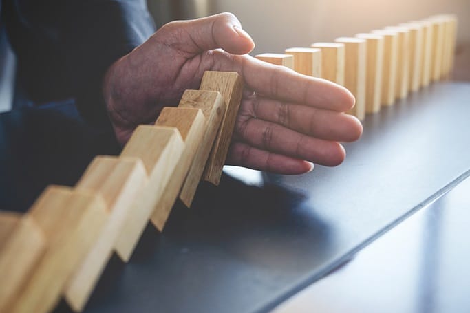 Close up of businessman's hand stopping falling dominoes.