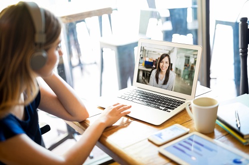 Woman wearing headphones and participating in a video conference call on a laptop while telecommuting from home