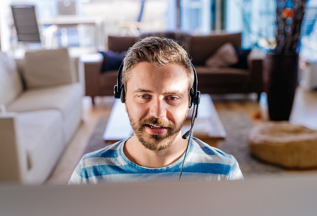 Man sitting at the desk, working from home on computer, wearing headseat, talking