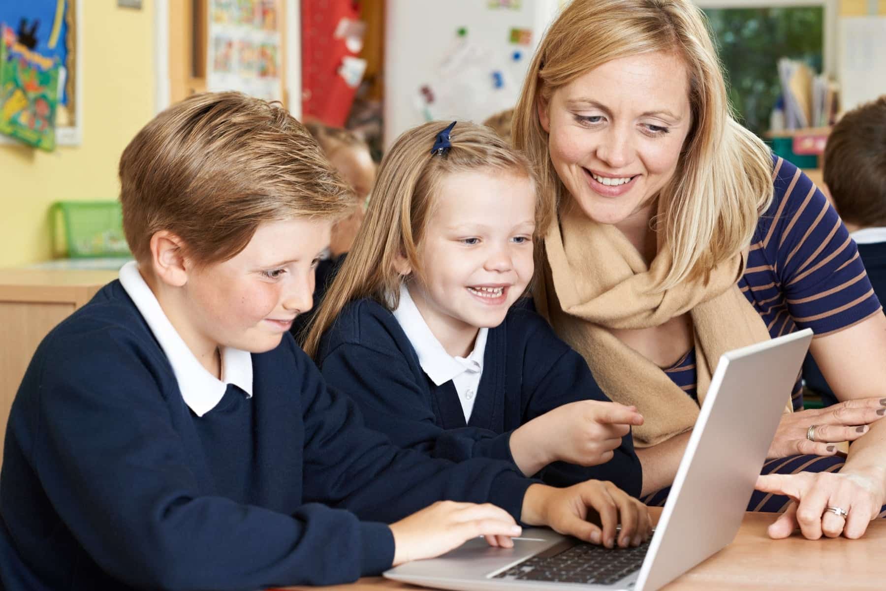 Two children and a teacher using laptops for schools, smiling.